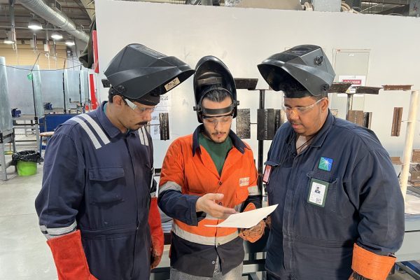 Trainees in welding masks reviewing a work instruction sheet